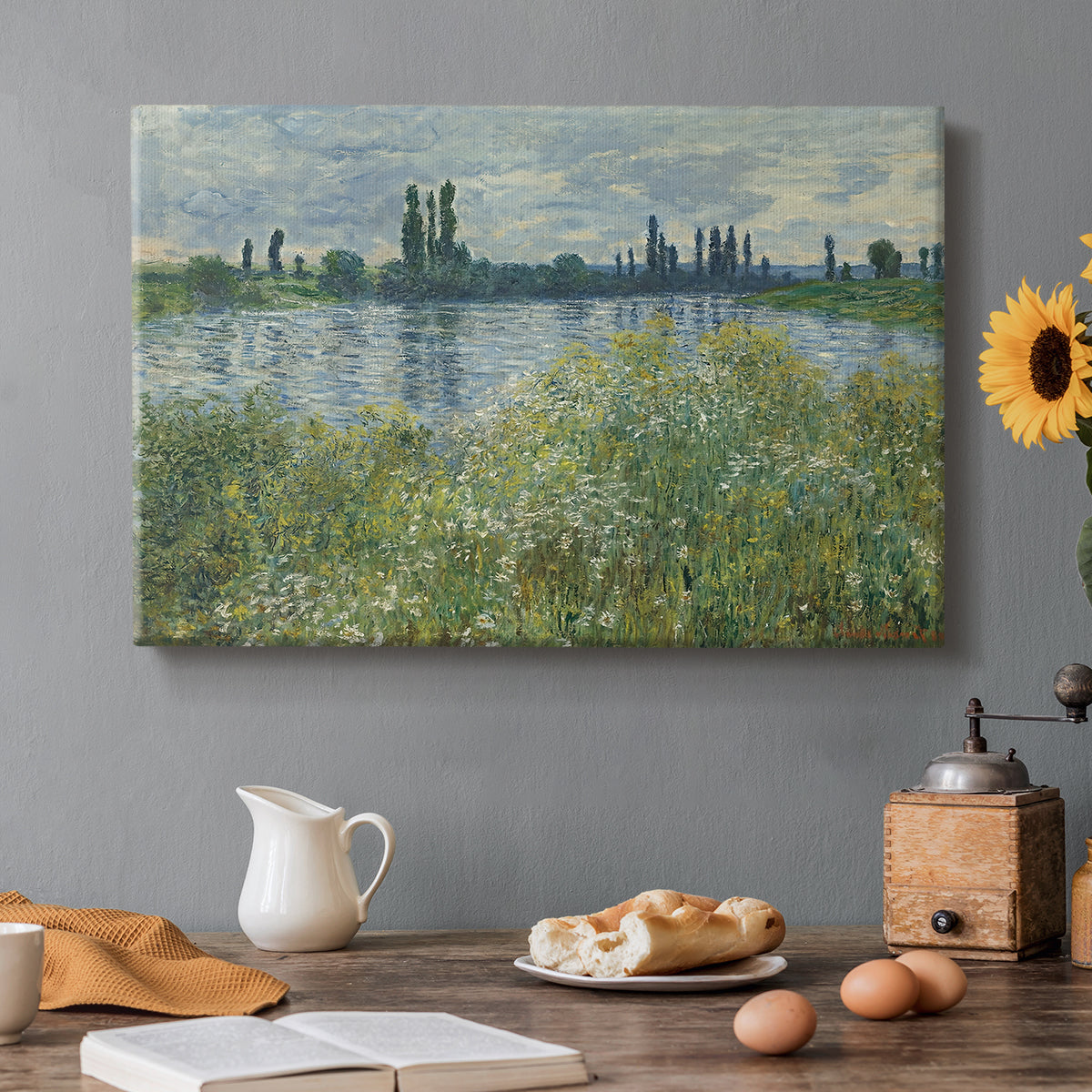 Canvas art print featuring a riverbank landscape with water, trees, and distant village buildings, set in a cozy kitchen setting