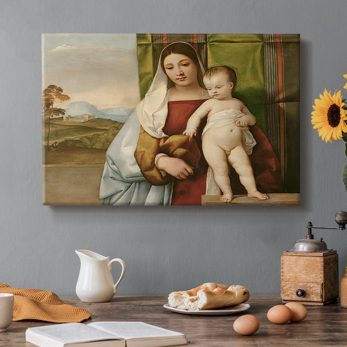Canvas art print featuring Madonna seated outdoors holding child beside dark tree and open sky, set in a cozy kitchen setting