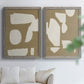 Set of two gray barnwood framed canvas prints depicting flat blocky forms, rough painted edges, and strong negative space arranged across two complementary compositions above a sofa in a bright living space.