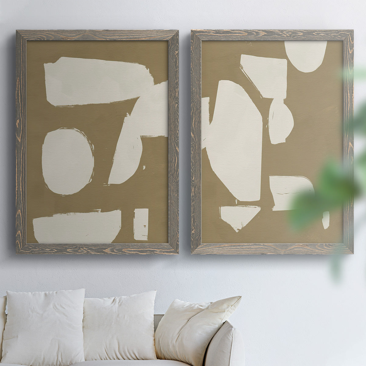 Set of two gray barnwood framed canvas prints depicting flat blocky forms, rough painted edges, and strong negative space arranged across two complementary compositions above a sofa in a bright living space.
