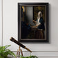 Quiet interior genre scene of a woman with scales by Johannes Vermeer in an ornate black frame with gilded inner detail displayed in a light-toned interior setting.