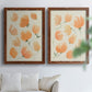 Set of two maple barnwood framed canvas prints depicting soft petals, thin black stems, and warm cream backgrounds arranged across two complementary compositions above a sofa in a bright living space.