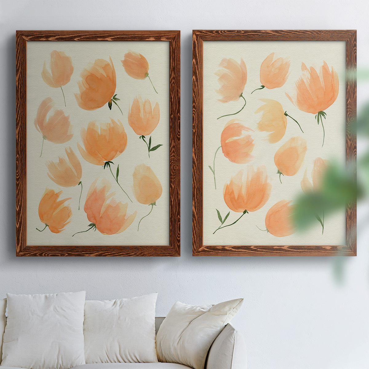 Set of two maple barnwood framed canvas prints depicting soft petals, thin black stems, and warm cream backgrounds arranged across two complementary compositions above a sofa in a bright living space.