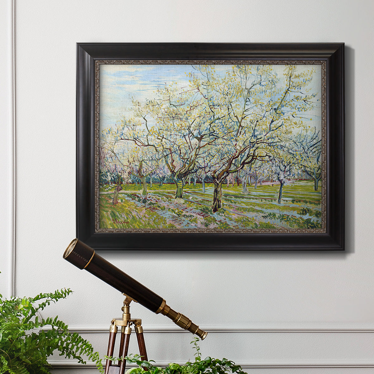Impressionist white-blossomed orchard landscape by Vincent van Gogh in an ornate black frame with gilded inner detail displayed in a light-toned interior setting.