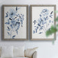 Set of two gray barnwood framed canvas prints depicting indigo blossoms, gestural blue leaves, and airy white space arranged across two complementary compositions above a sofa in a bright living space.