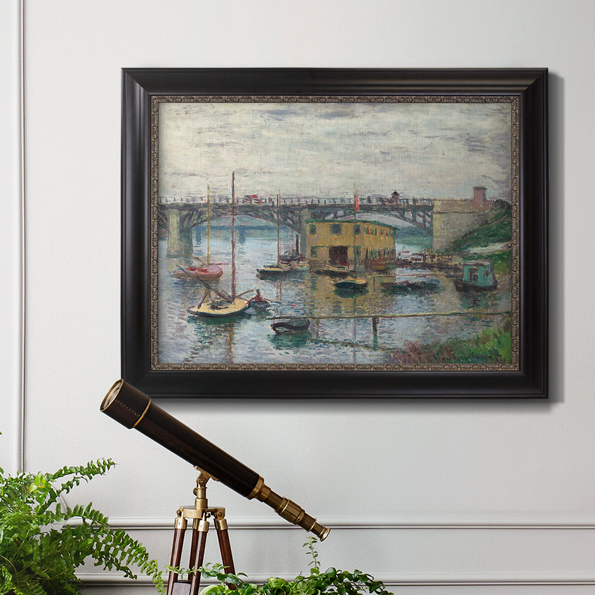 Impressionist river bridge scene on an overcast day by Claude Monet in an ornate black frame with gilded inner detail displayed in a light-toned interior setting.
