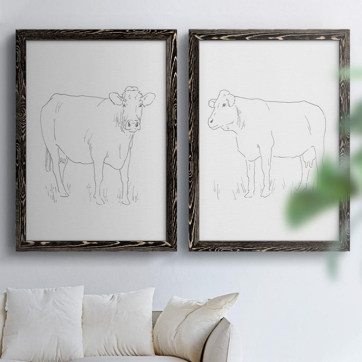 Set of two black barnwood framed canvas prints depicting fine gray lines, white backgrounds, and quiet farm-animal profiles arranged across two complementary compositions above a sofa in a bright living space.