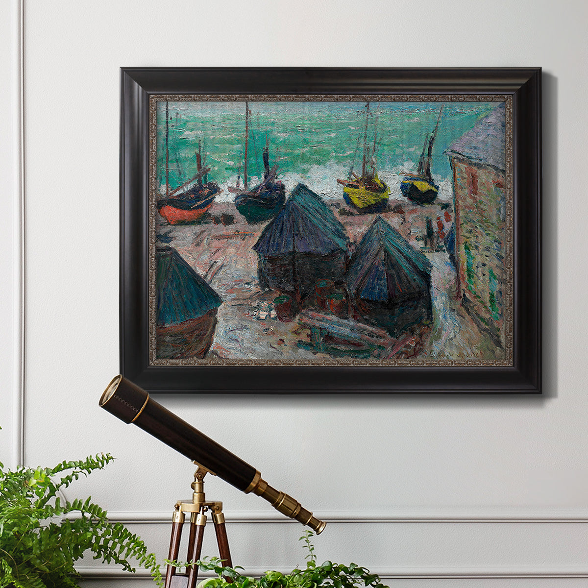 Impressionist coastal beach scene with boats by Claude Monet in an ornate black frame with gilded inner detail displayed in a light-toned interior setting.