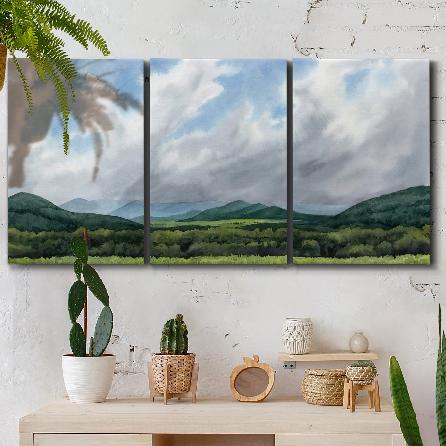 Three-panel canvas wall art featuring pastoral mountain landscape in blue, displayed in a boho-chic entryway above a console table.