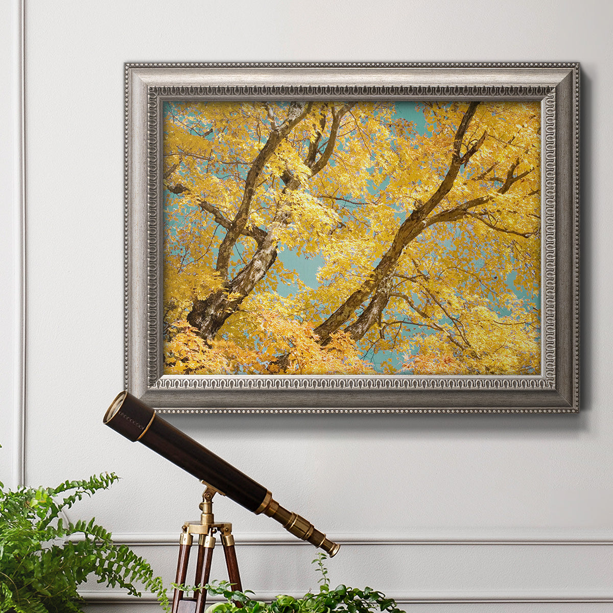 Vibrant yellow autumn leaves on branches in an ornate vintage silver frame displayed in a light-toned interior setting.