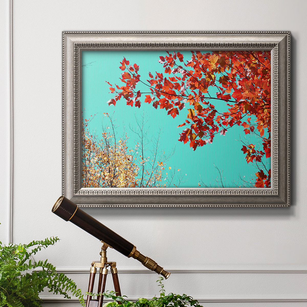 Red autumn leaves against a blue sky in an ornate vintage silver frame displayed in a light-toned interior setting.