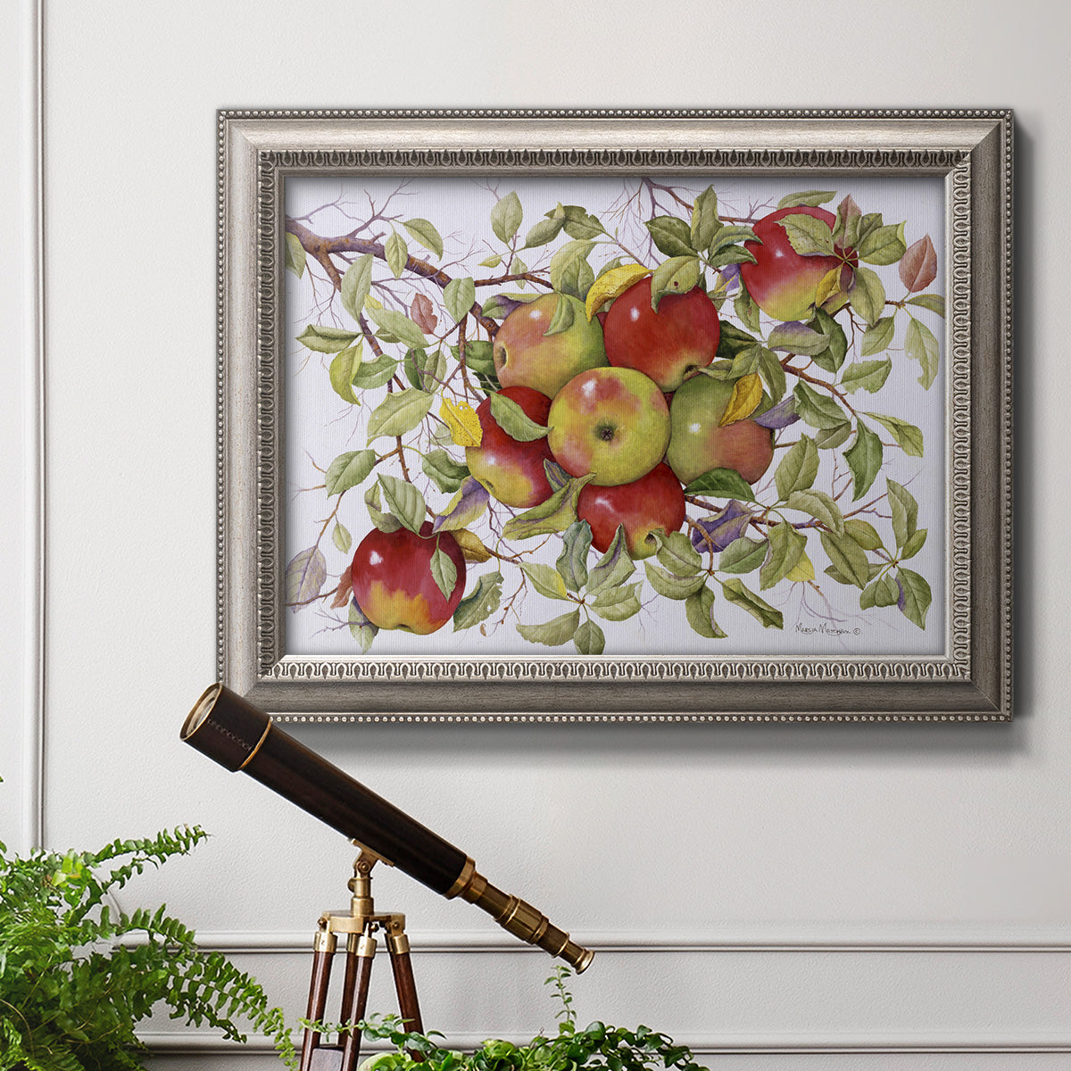Classic still life painting of apples in an ornate vintage silver frame displayed in a light-toned interior setting.