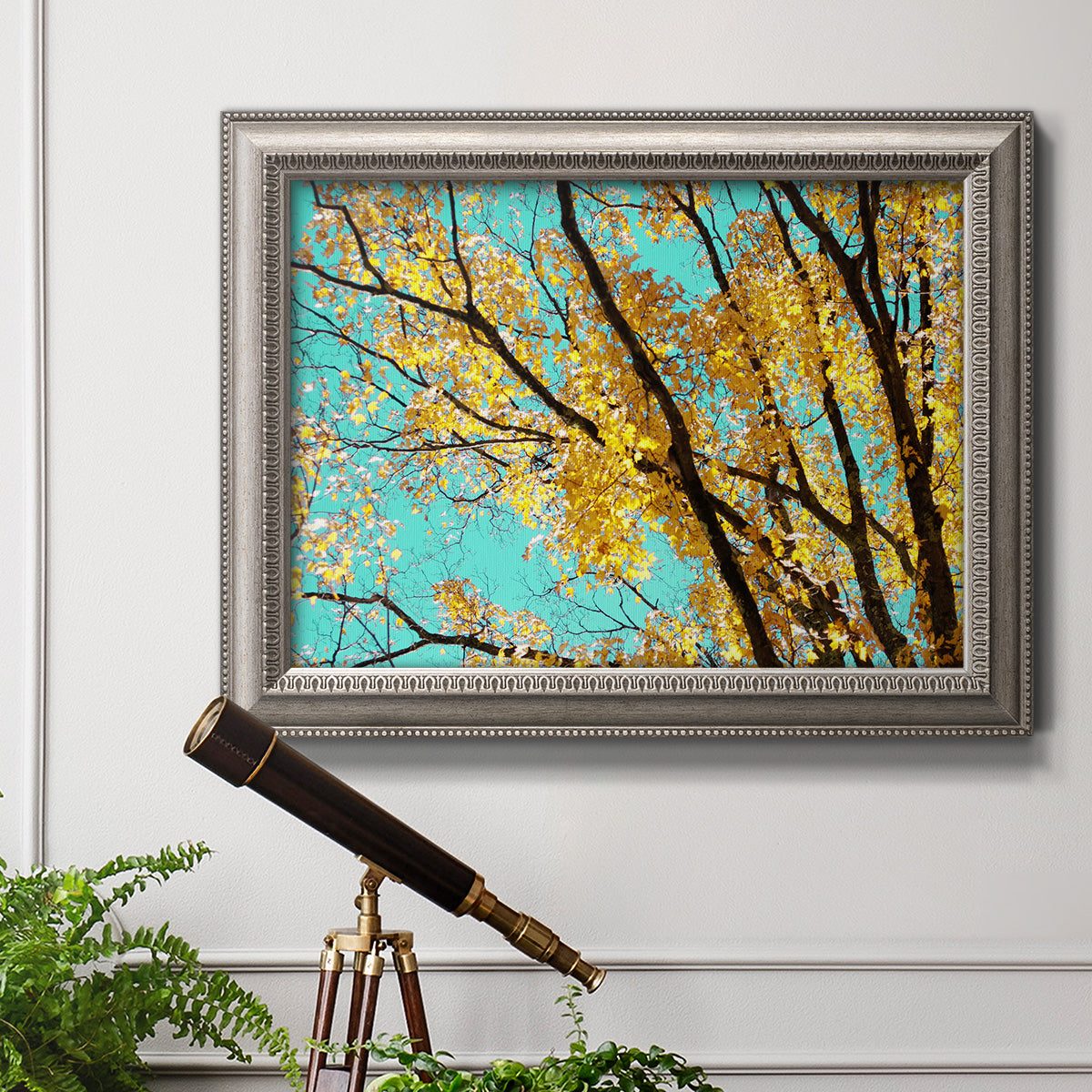Bright autumn leaves against a blue sky in an ornate vintage silver frame displayed in a light-toned interior setting.