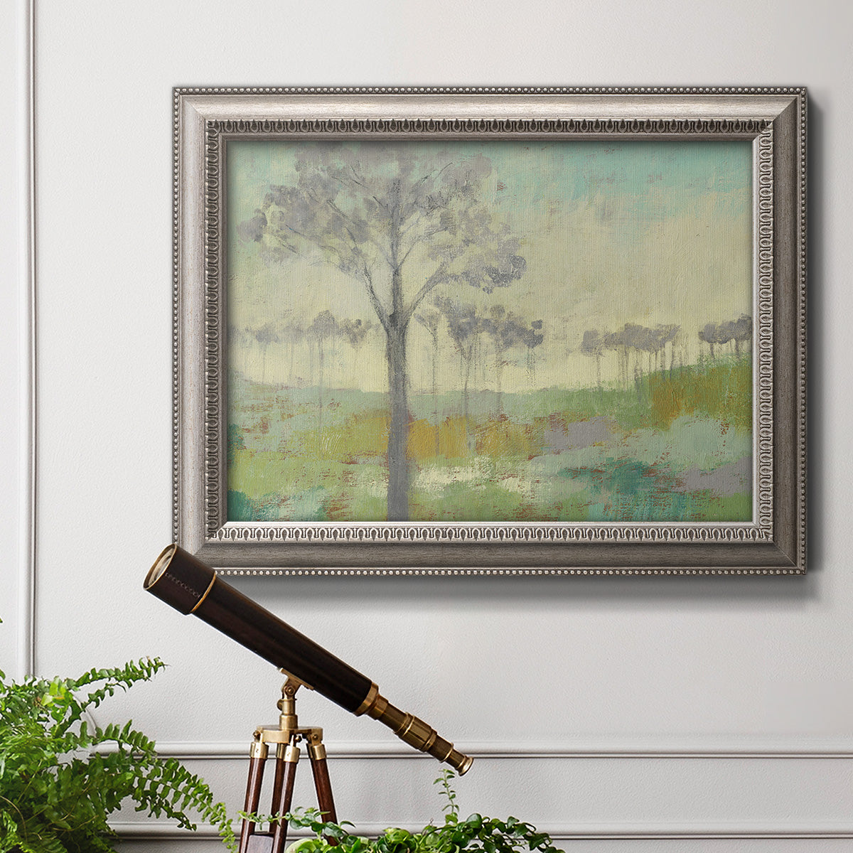 Traditional watercolor tree landscape artwork in an ornate vintage silver frame displayed in a light-toned interior setting.