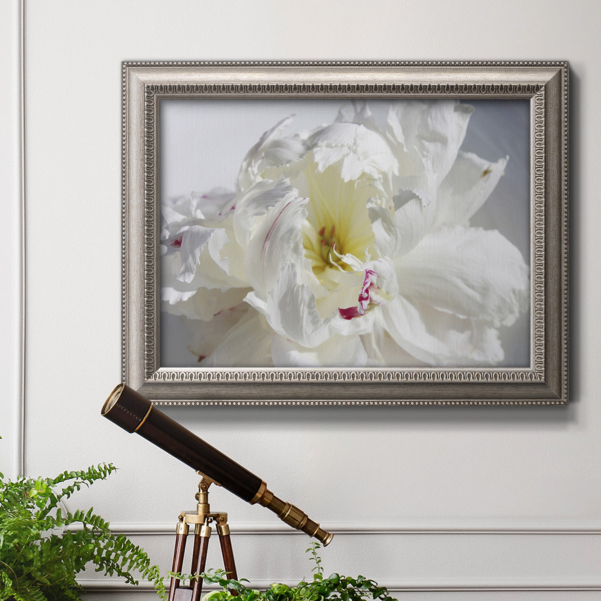 Soft white peony close-up in an ornate vintage silver frame displayed in a light-toned interior setting.