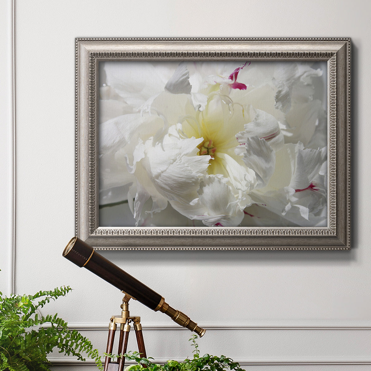 Close up view of peony petals in an ornate vintage silver frame displayed in a light-toned interior setting.