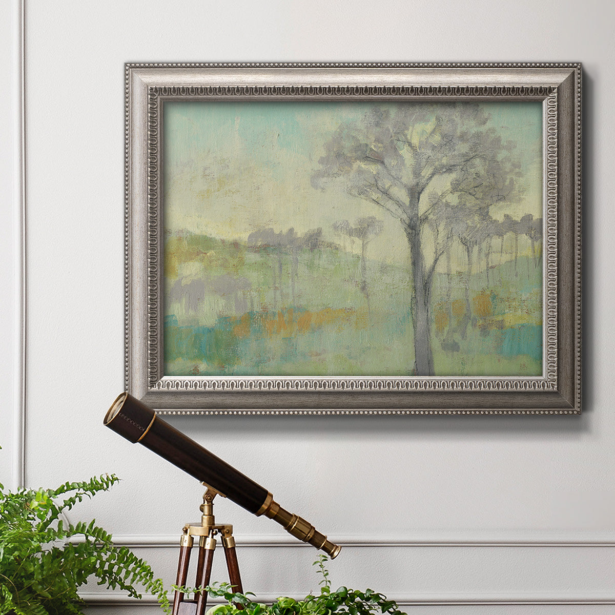 Classical watercolor landscape with trees in an ornate vintage silver frame displayed in a light-toned interior setting.