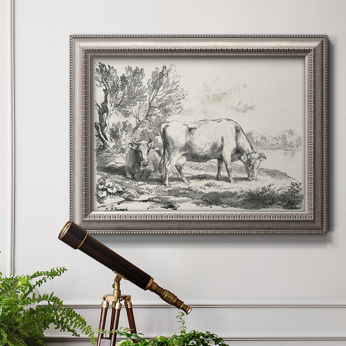 Traditional rural landscape scene by Nicolas Berchem in an ornate vintage silver frame displayed in a light-toned interior setting.