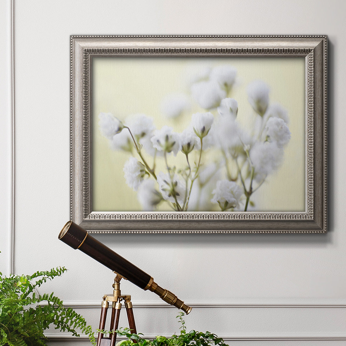 Soft-focus baby’s breath flower photograph in an ornate vintage silver frame displayed in a light-toned interior setting.