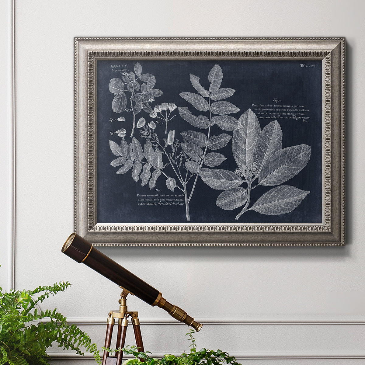 Antique botanical foliage artwork on navy background in an ornate vintage silver frame displayed in a light-toned interior setting.