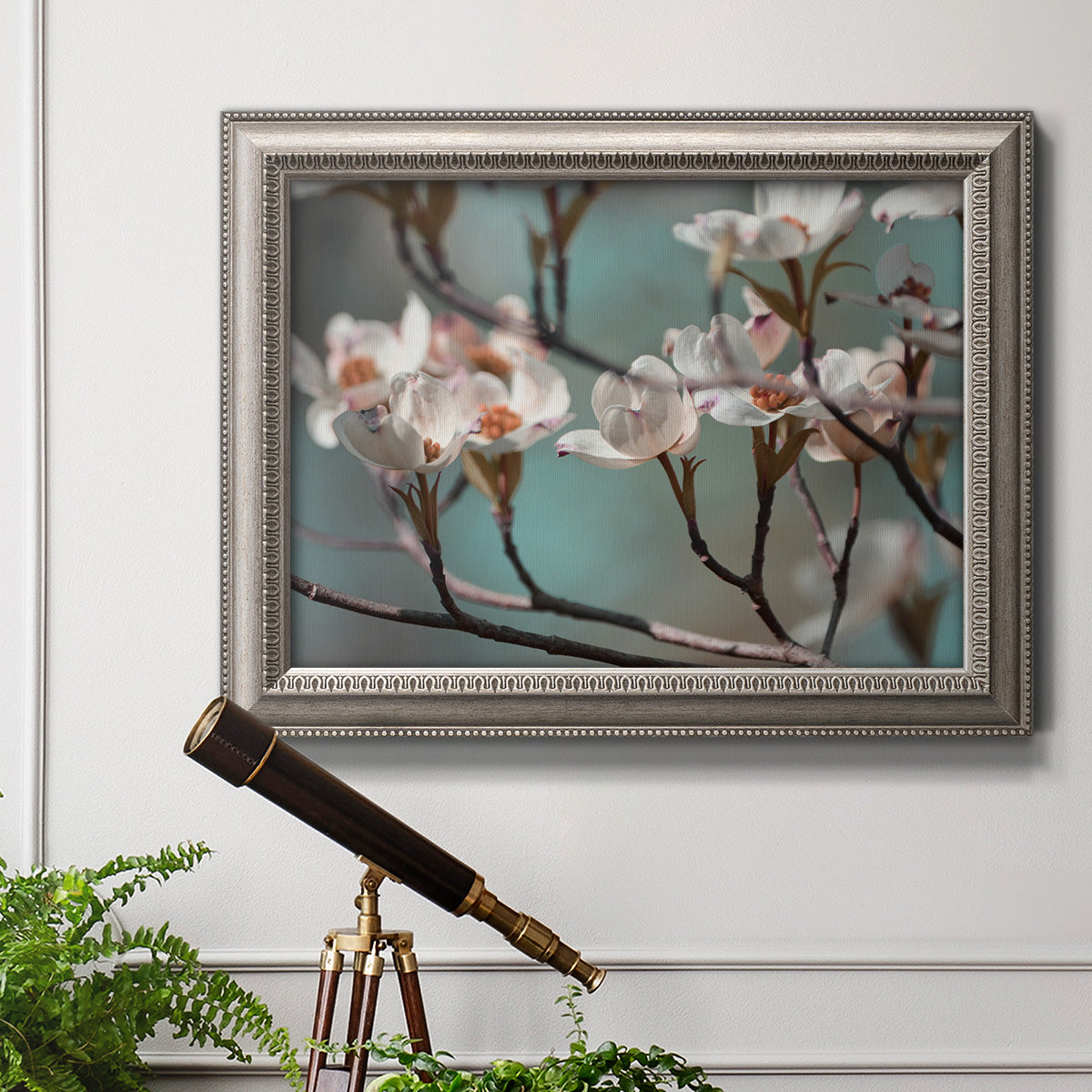 Close-up dogwood blossom photography in an ornate vintage silver frame displayed in a light-toned interior setting.