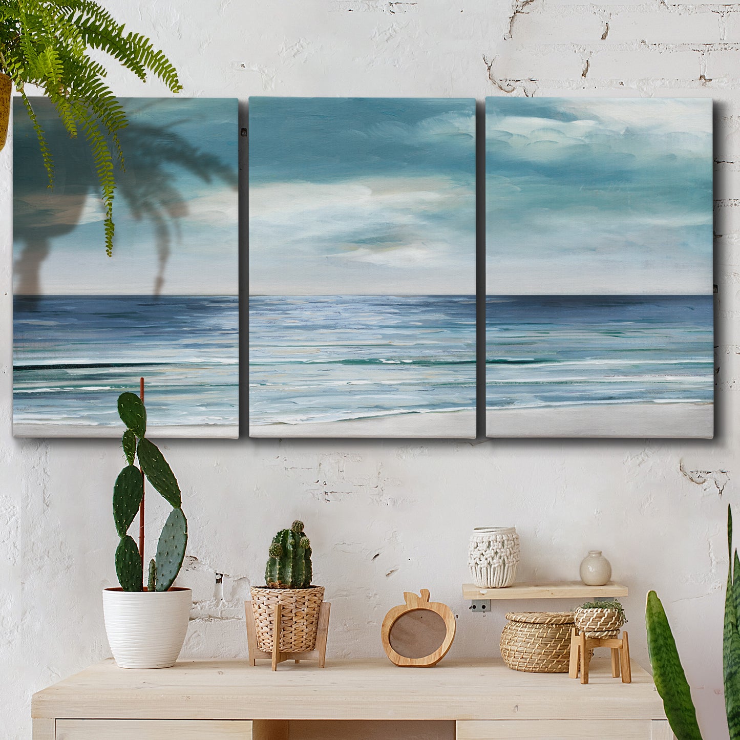 Three-panel canvas wall art featuring calm coastal shoreline, displayed in a boho-chic entryway above a console table.