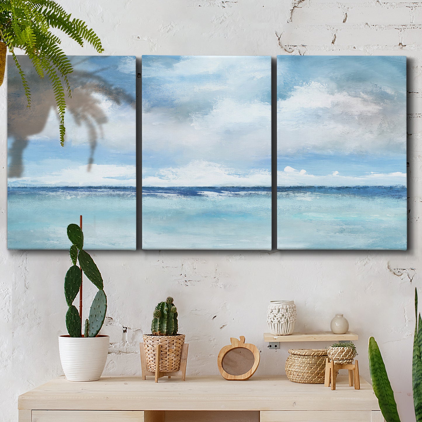 Three-panel canvas wall art featuring tropical clouds over ocean horizon, displayed in a boho-chic entryway above a console table.