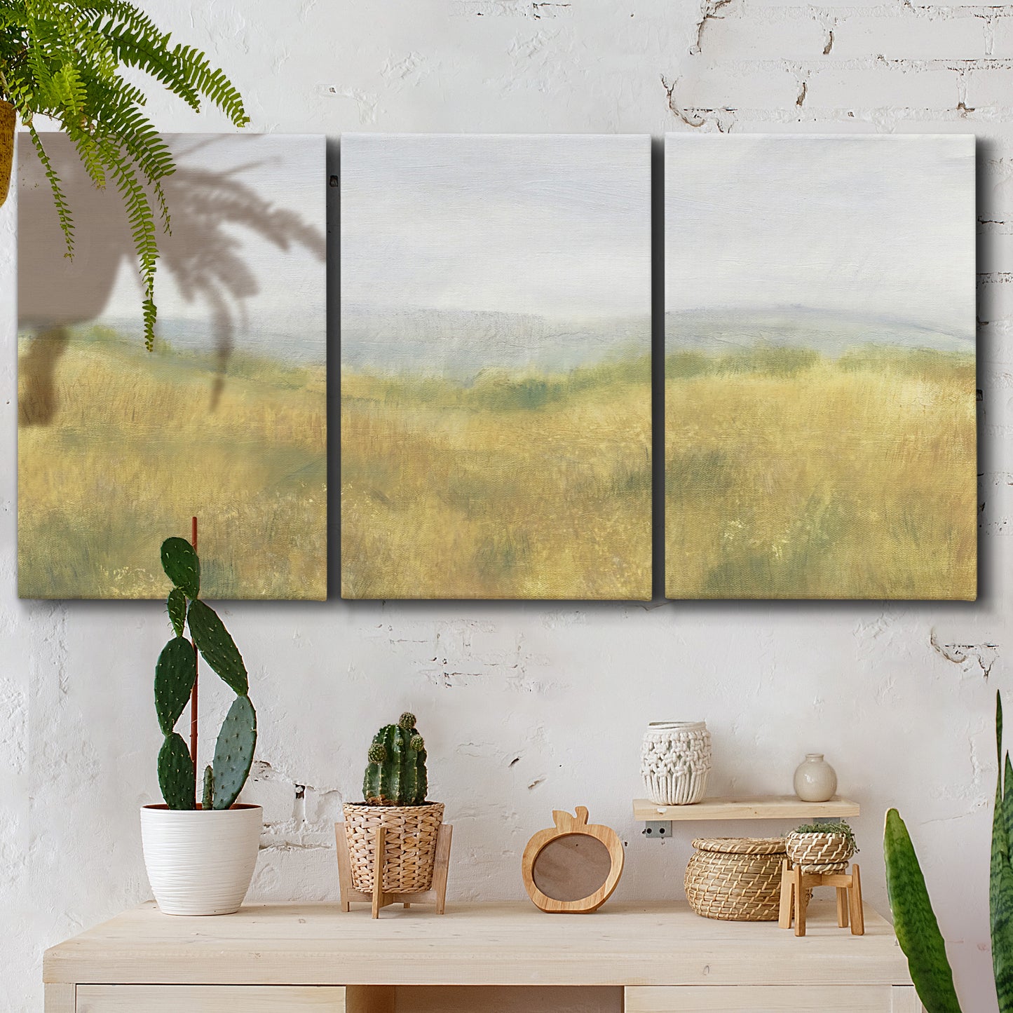 Three-panel canvas wall art featuring pastoral wheat field landscape, displayed in a boho-chic entryway above a console table.