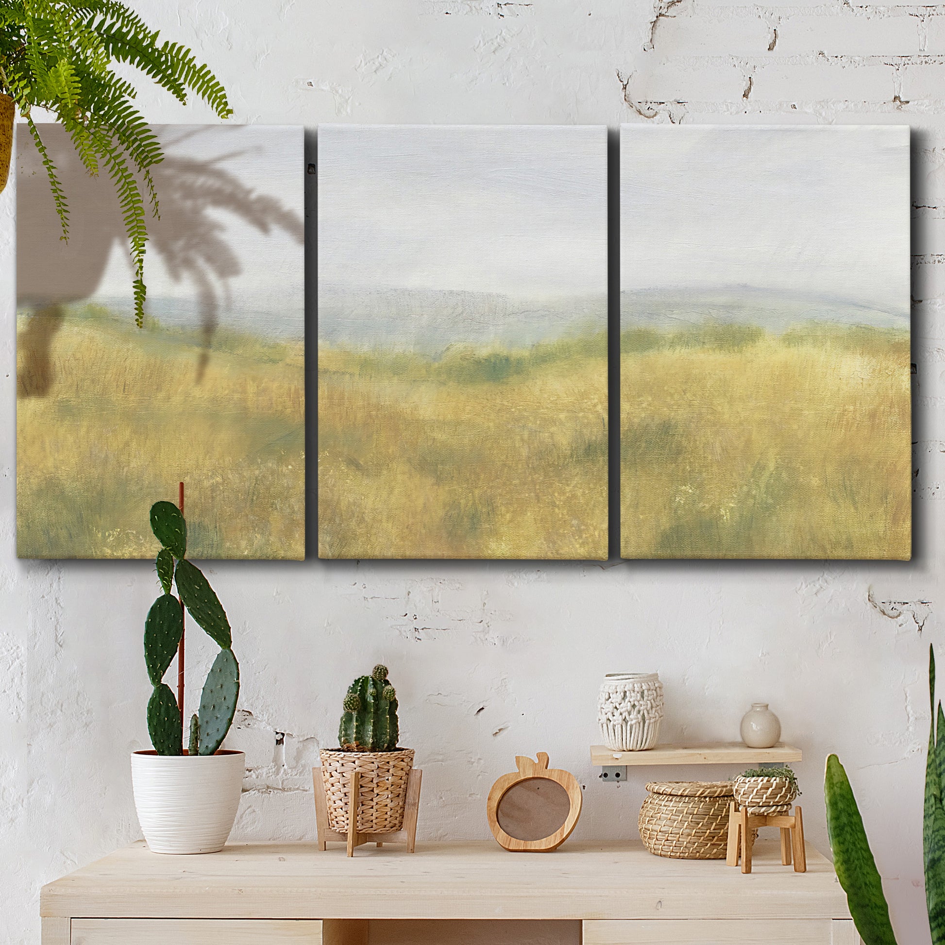Three-panel canvas wall art featuring pastoral wheat field landscape, displayed in a boho-chic entryway above a console table.