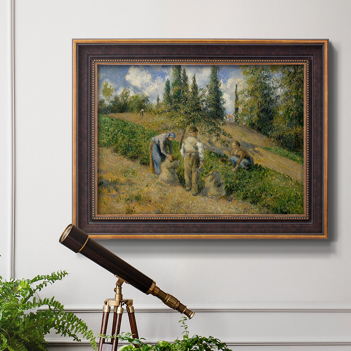 Impressionist countryside harvest scene by Camille Pissarro in an ornate bronzed mahogany wood frame displayed in a light-toned interior setting.