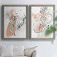 Set of two gray barnwood framed canvas prints depicting scribbled petals, translucent washes, and drifting stems arranged across two complementary compositions above a sofa in a bright living space.