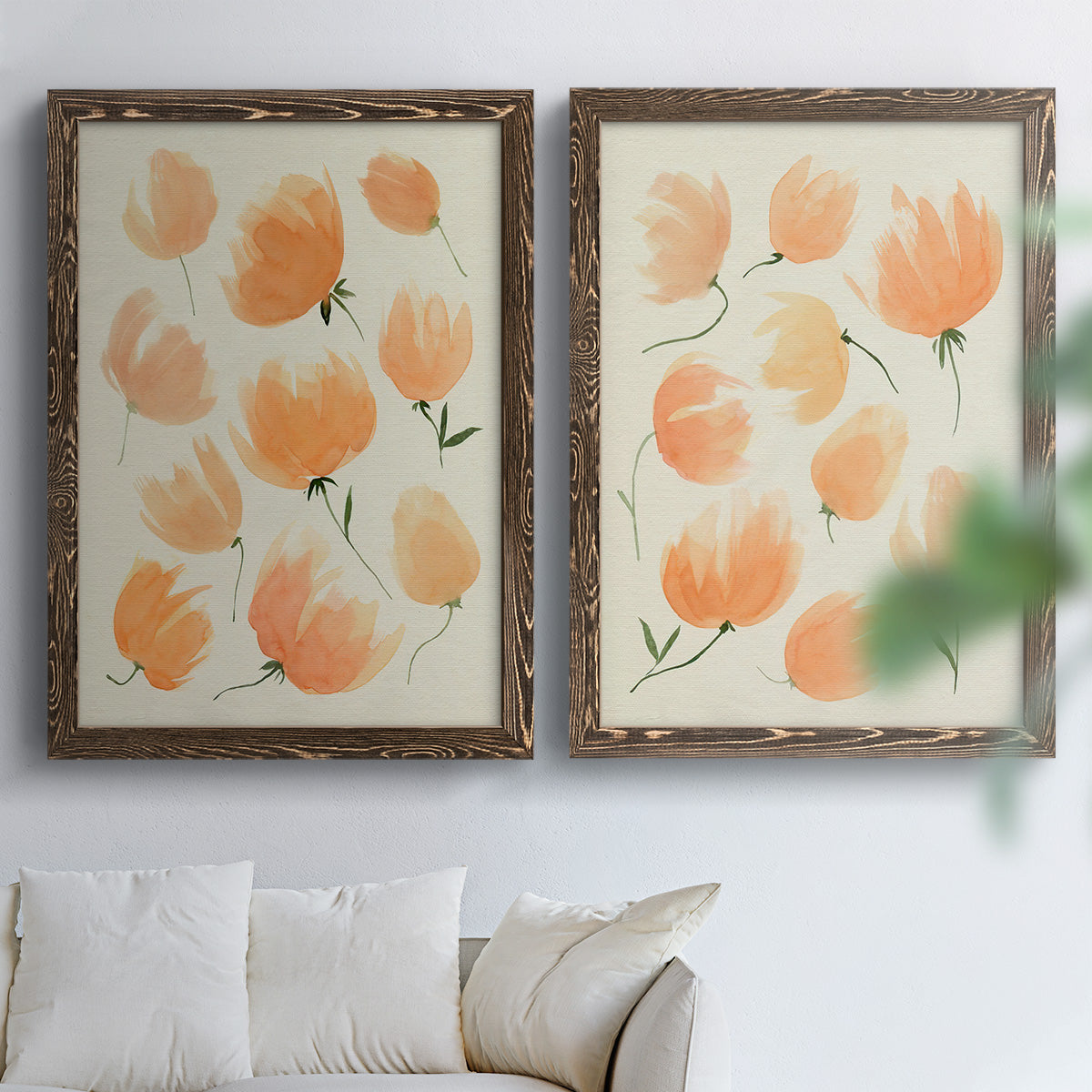 Set of two walnut barnwood framed canvas prints depicting soft petals, thin black stems, and warm cream backgrounds arranged across two complementary compositions above a sofa in a bright living space.