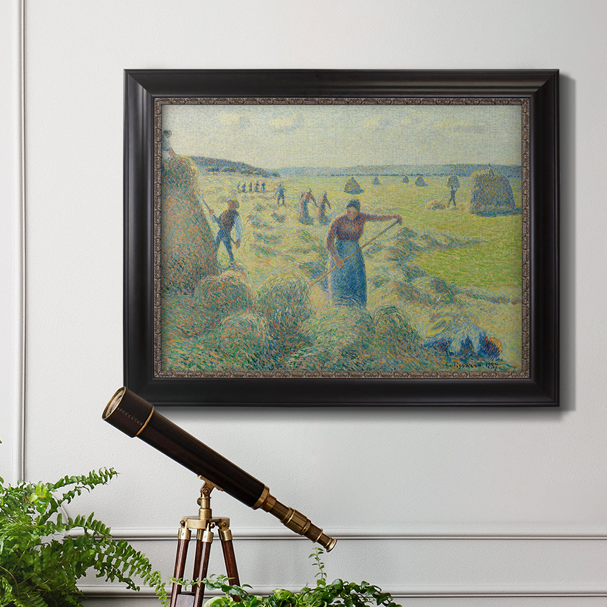Impressionist rural hay harvest landscape by Camille Pissarro in an ornate black frame with gilded inner detail displayed in a light-toned interior setting.
