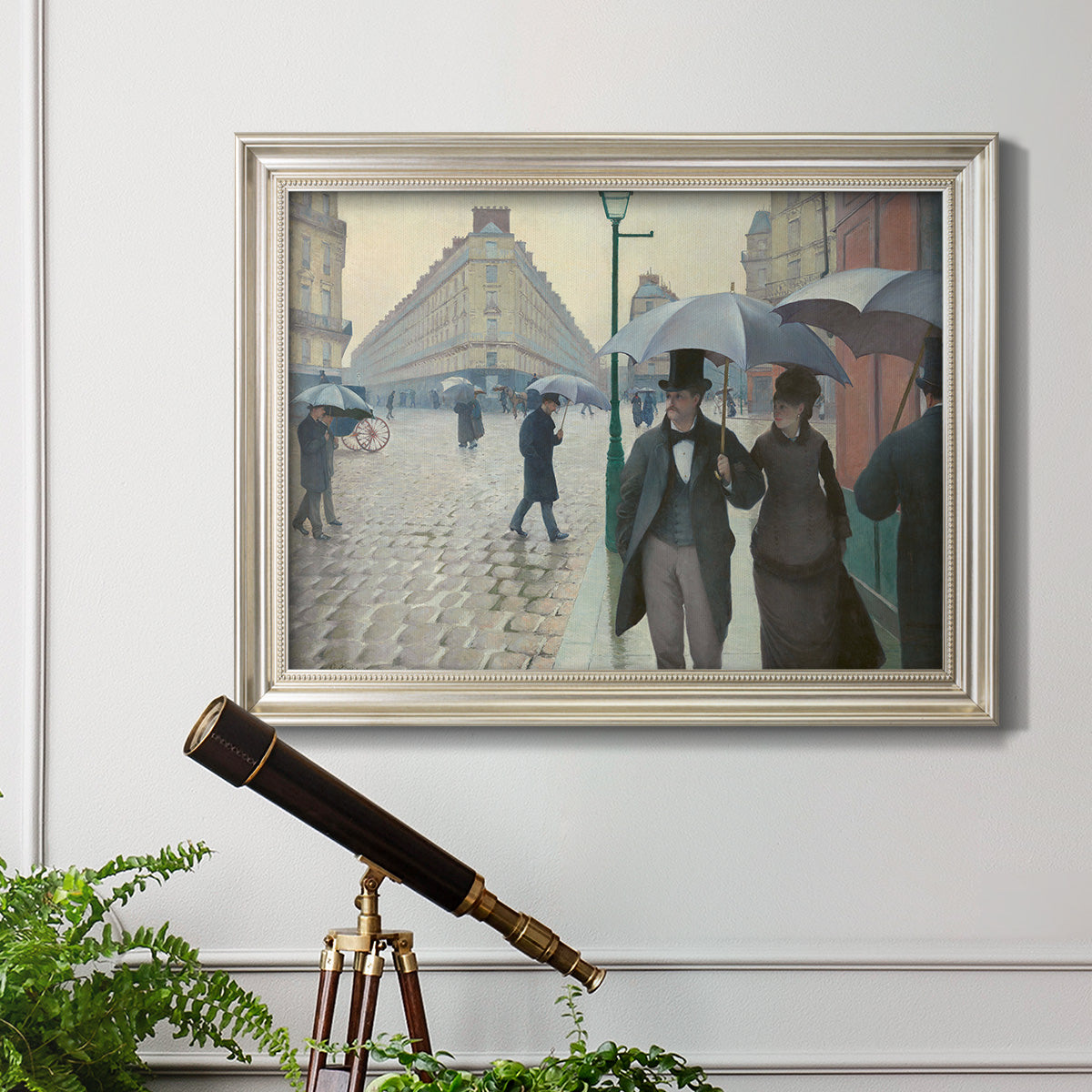 Impressionist urban street scene in the rain by Gustave Caillebotte in an ornate champagne frame displayed in a light-toned interior setting.