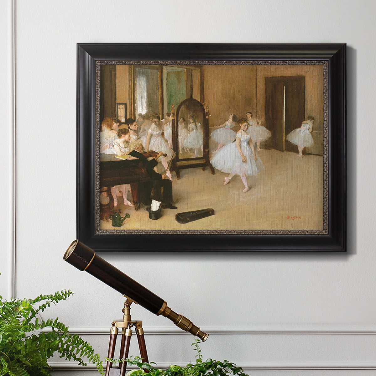 Impressionist dance class interior scene by Edgar Degas in an ornate black frame with gilded inner detail displayed in a light-toned interior setting.