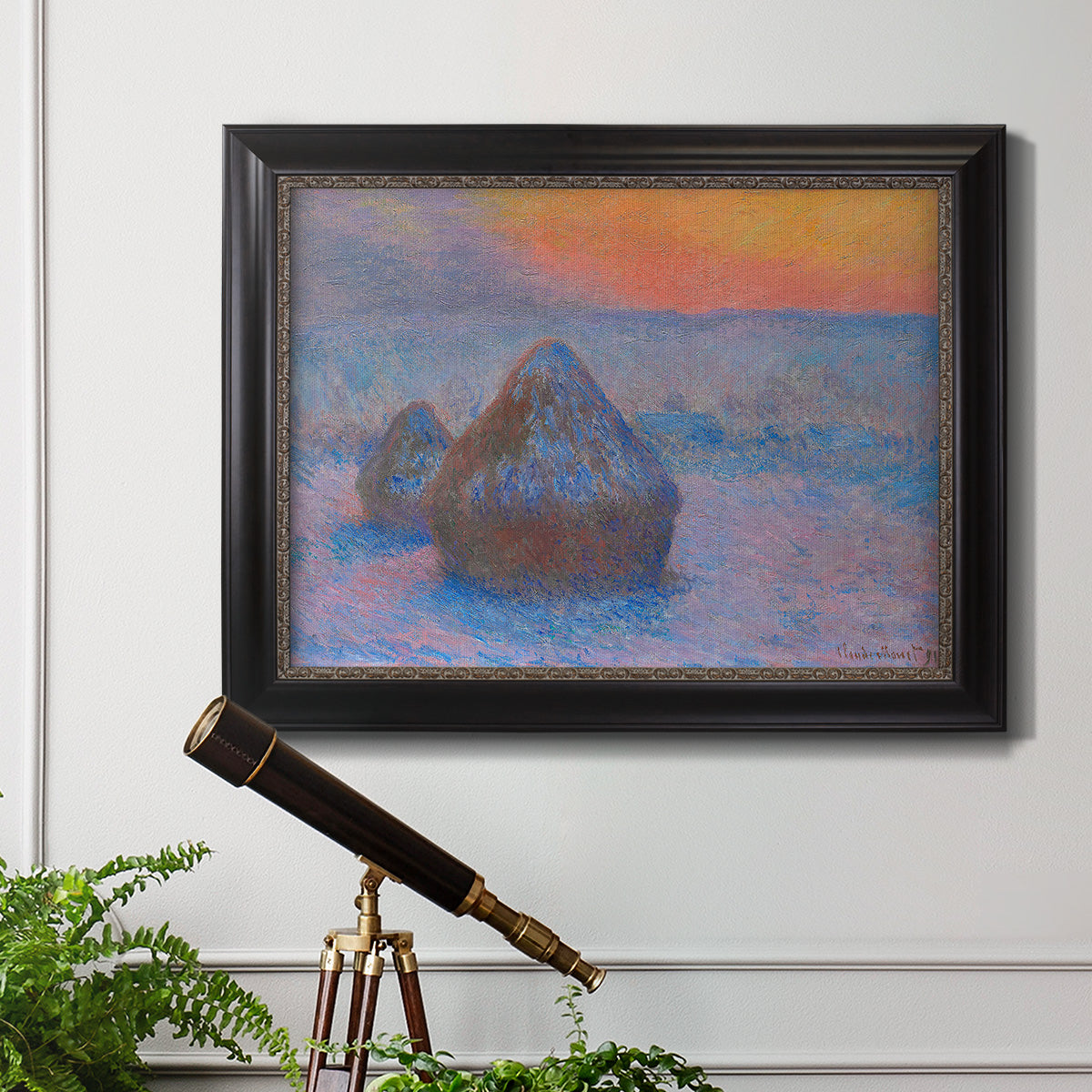Impressionist haystack scene at sunset by Claude Monet in an ornate black frame with gilded inner detail displayed in a light-toned interior setting.