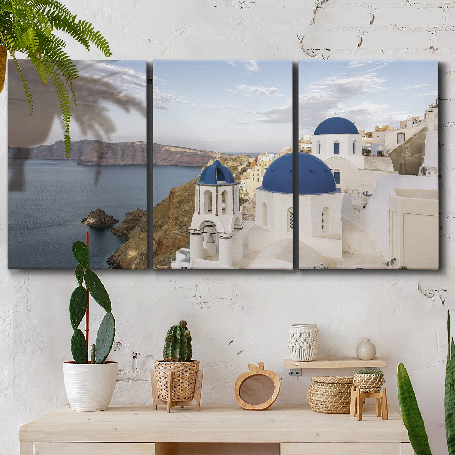 Three-panel canvas wall art featuring white buildings overlooking sea cliffs, displayed in a boho-chic entryway above a console table.