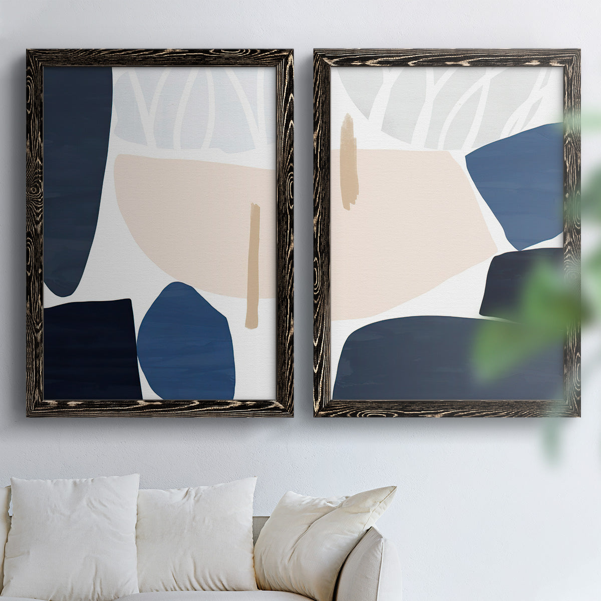 Set of two black barnwood framed canvas prints depicting rounded dark forms, pale sand fields, and clean modern edges arranged across two complementary compositions above a sofa in a bright living space.