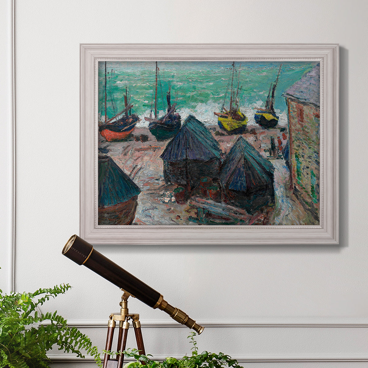 Impressionist coastal beach scene with boats by Claude Monet in an ornate weathered white frame displayed in a light-toned interior setting.