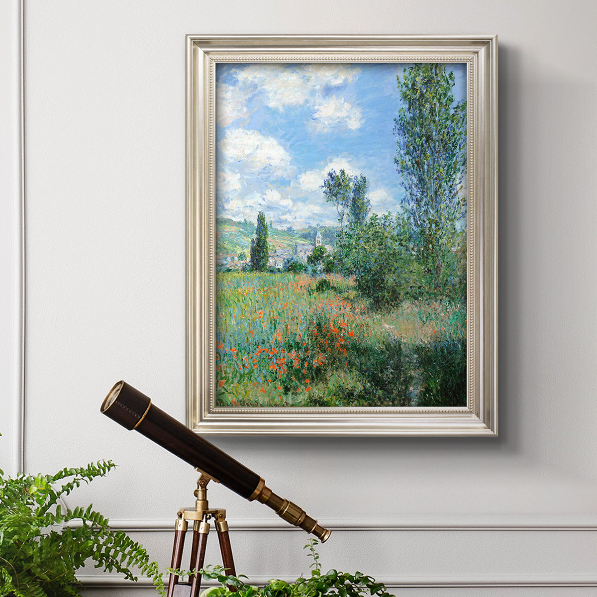 Impressionist pastoral landscape with poppy fields by Claude Monet in an ornate champagne frame displayed in a light-toned interior setting.