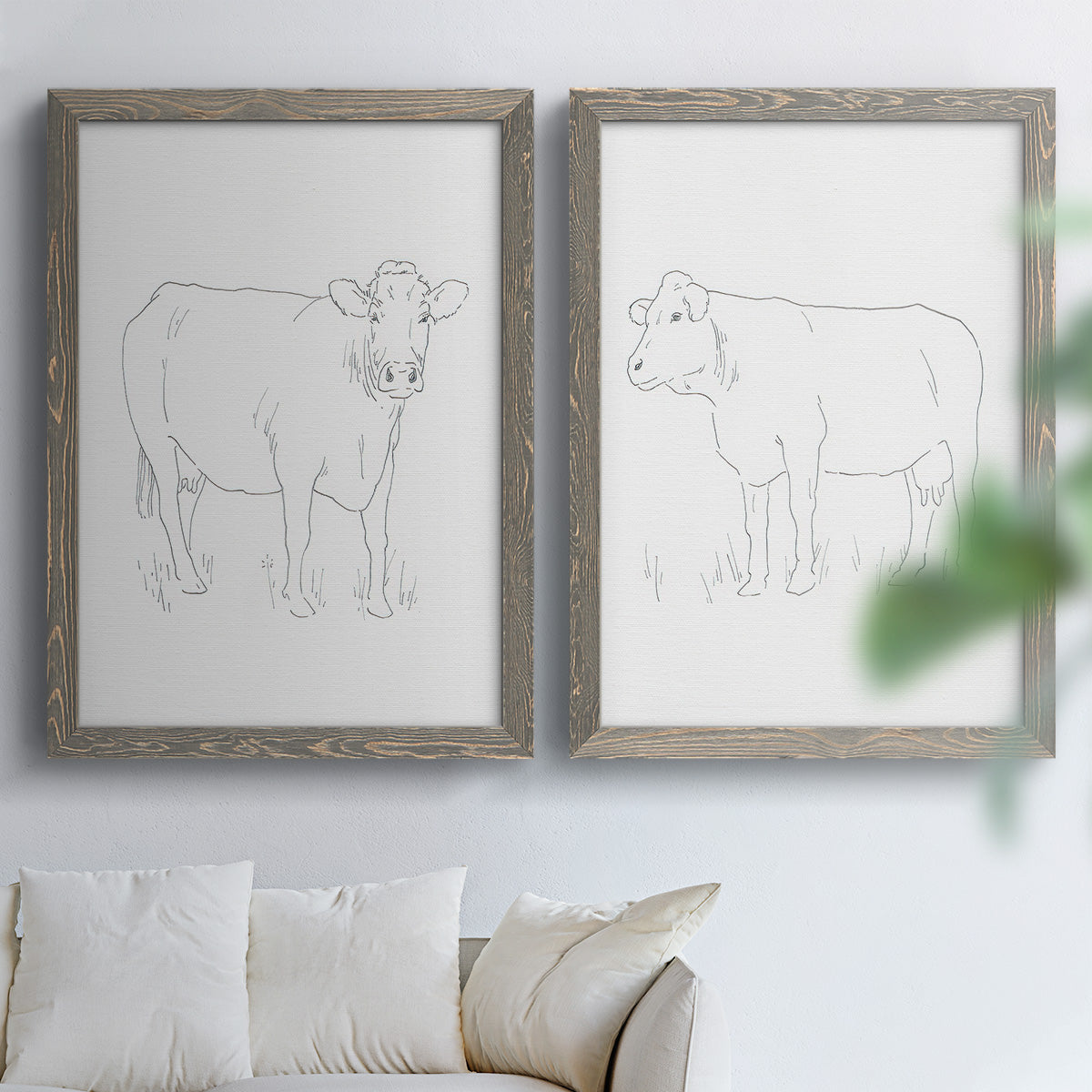 Set of two gray barnwood framed canvas prints depicting fine gray lines, white backgrounds, and quiet farm-animal profiles arranged across two complementary compositions above a sofa in a bright living space.