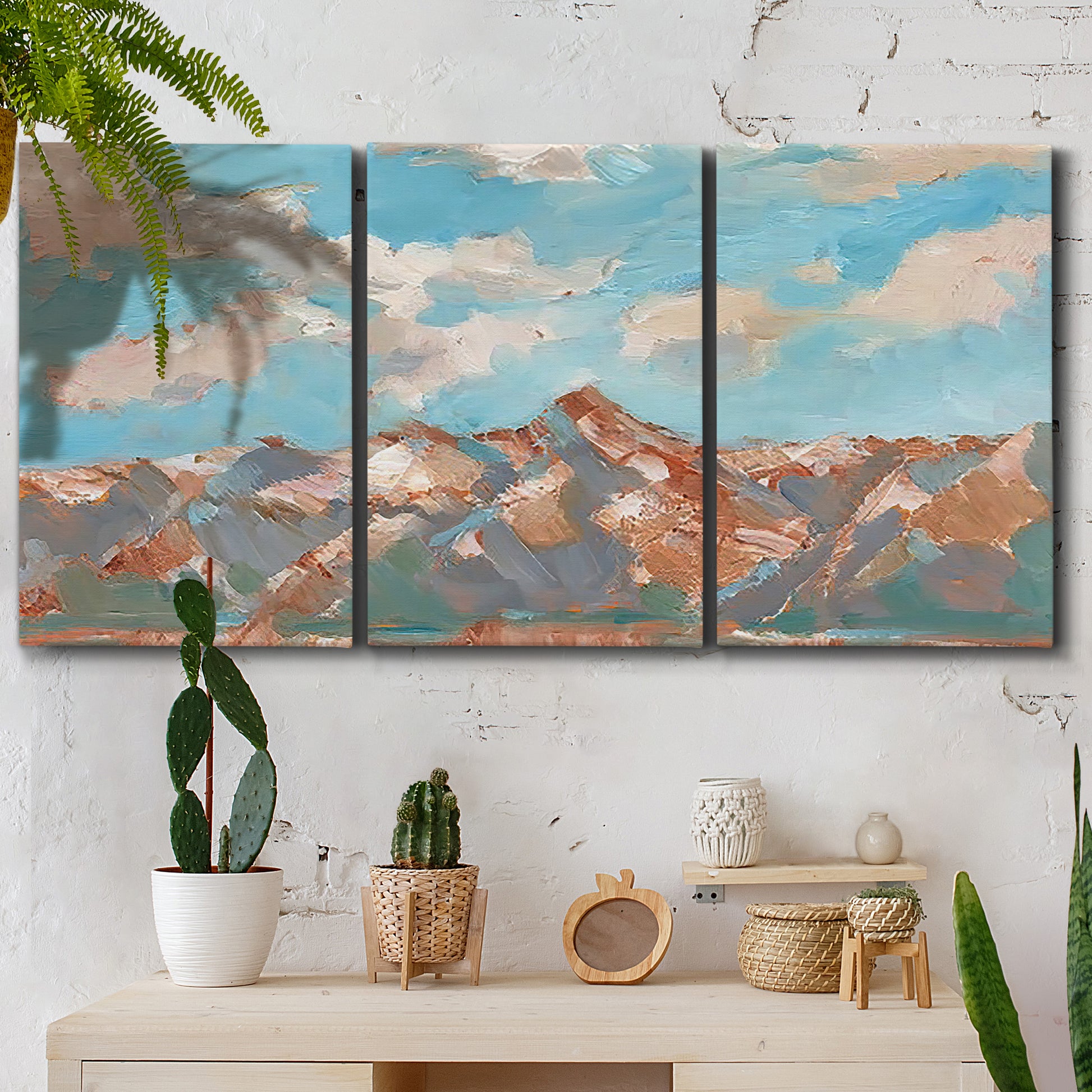 Three-panel canvas wall art featuring soft pastel western hills landscape, displayed in a boho-chic entryway above a console table.