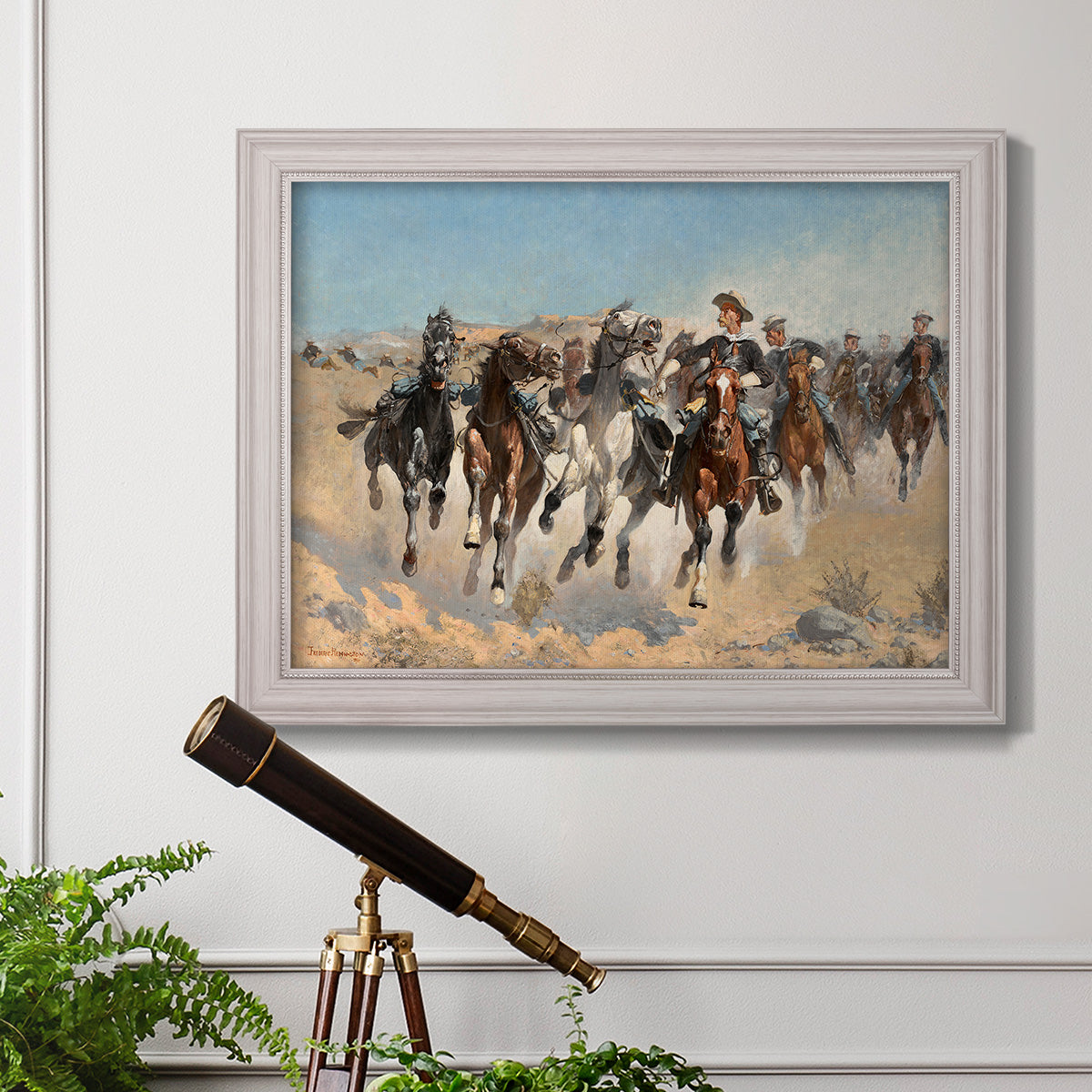 Impressionist western action scene by Frederic Remington in an ornate weathered white frame displayed in a light-toned interior setting.