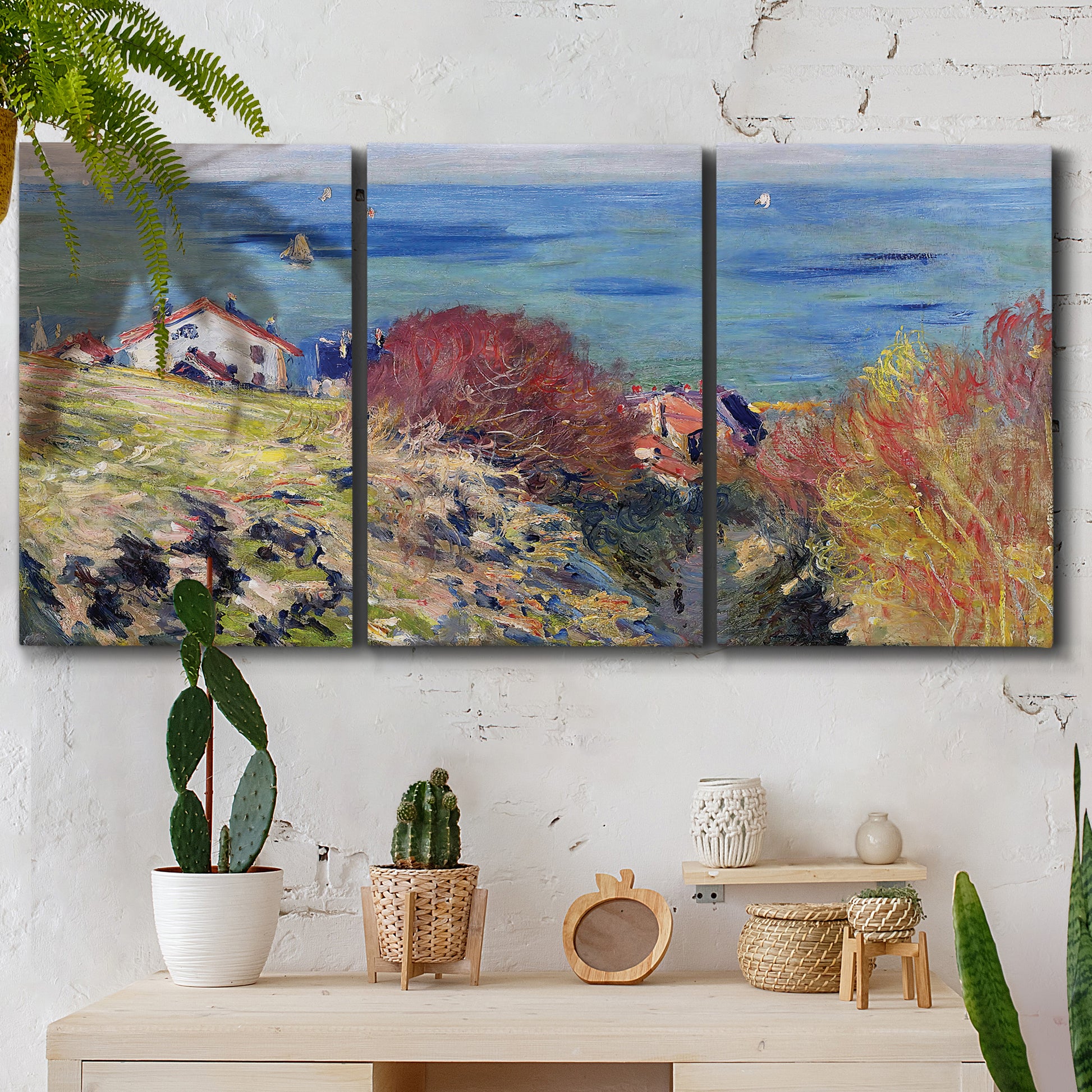 Three-panel canvas wall art featuring coastal village shoreline landscape, displayed in a boho-chic entryway above a console table.