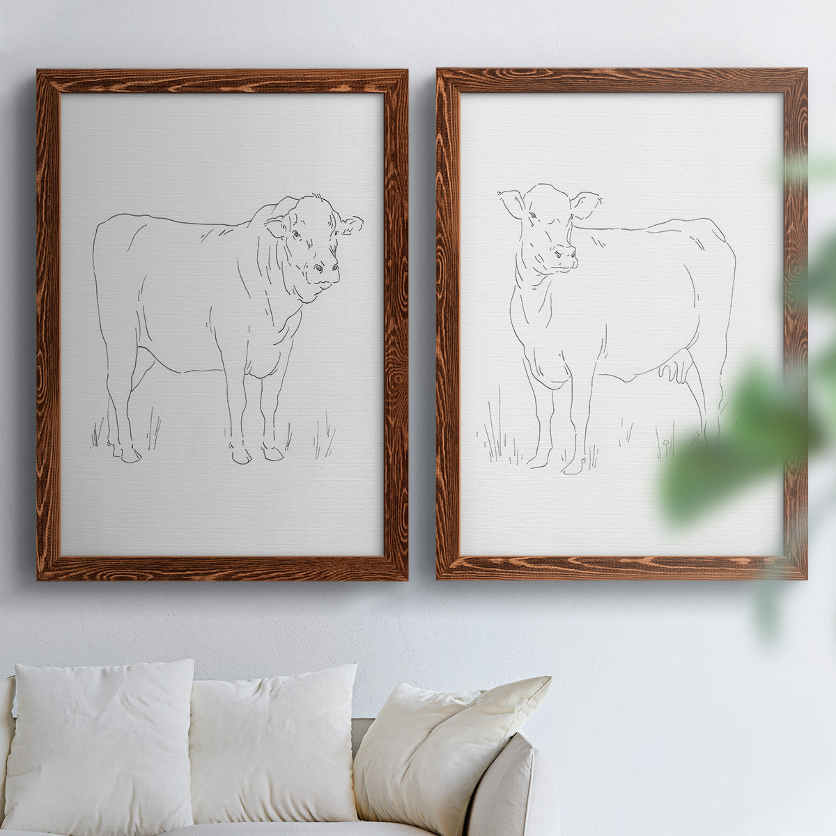Set of two maple barnwood framed canvas prints depicting fine gray lines, white backgrounds, and quiet farm-animal profiles arranged across two complementary compositions above a sofa in a bright living space.