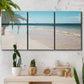 Three-panel canvas wall art featuring white sand beach with gentle waves, displayed in a boho-chic entryway above a console table.