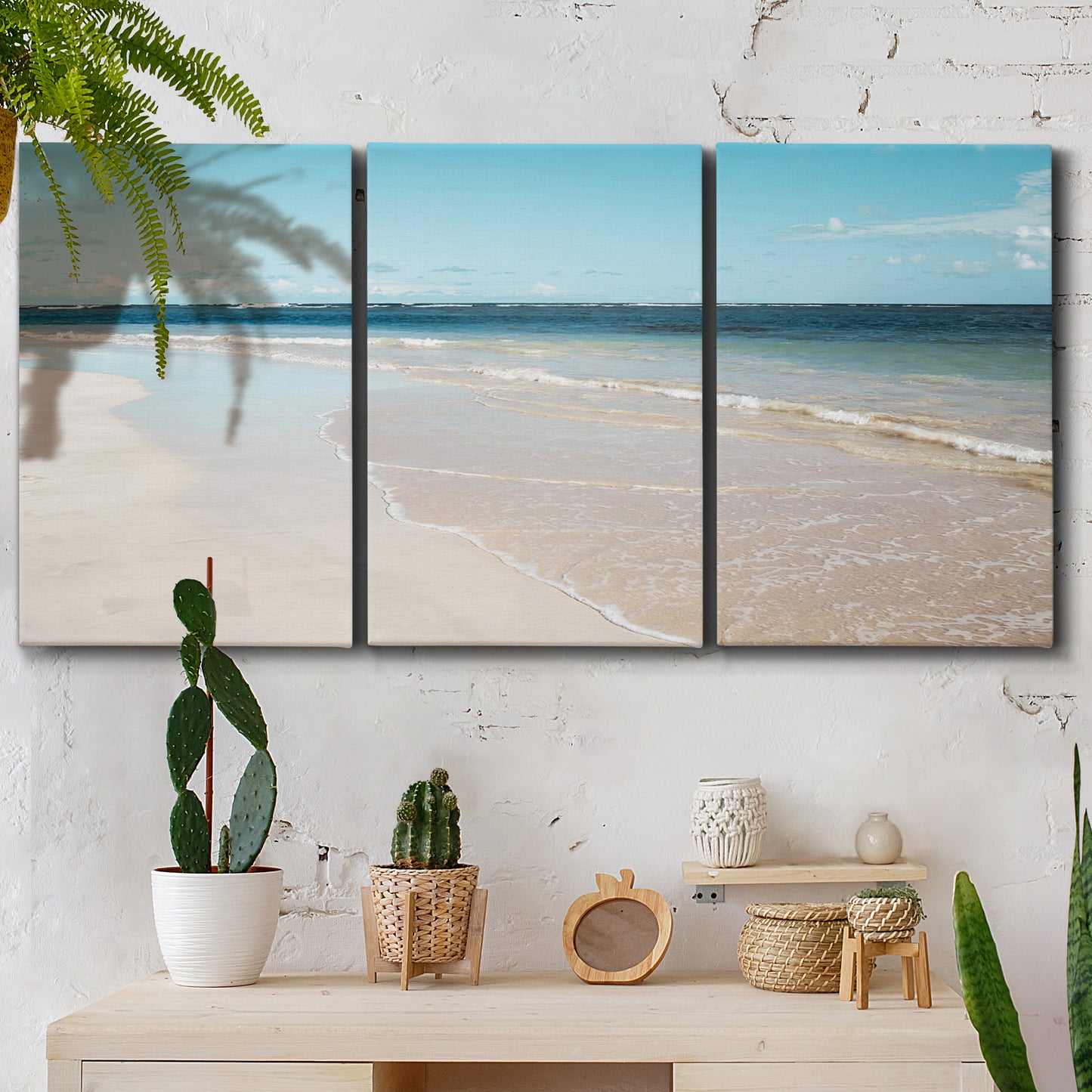 Three-panel canvas wall art featuring white sand beach with gentle waves, displayed in a boho-chic entryway above a console table.