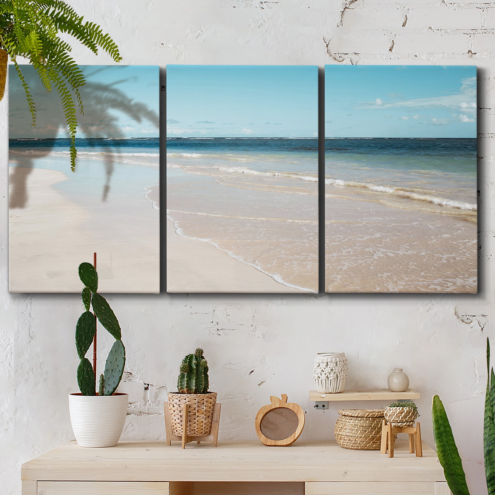 Three-panel canvas wall art featuring white sand beach with gentle waves, displayed in a boho-chic entryway above a console table.