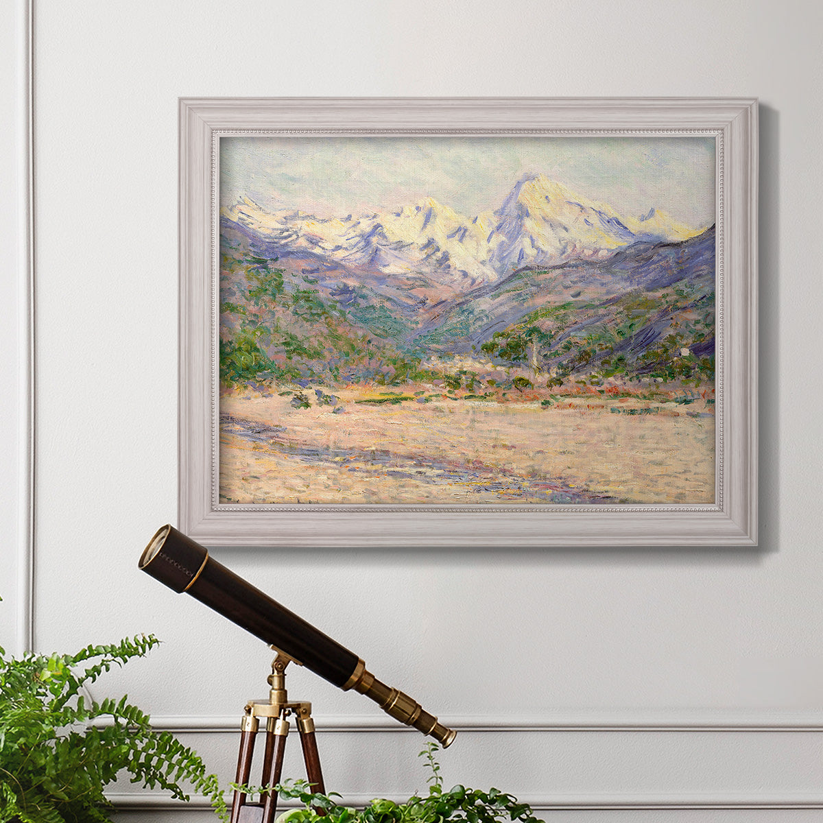 Impressionist valley landscape in southern France by Claude Monet in an ornate weathered white frame displayed in a light-toned interior setting.