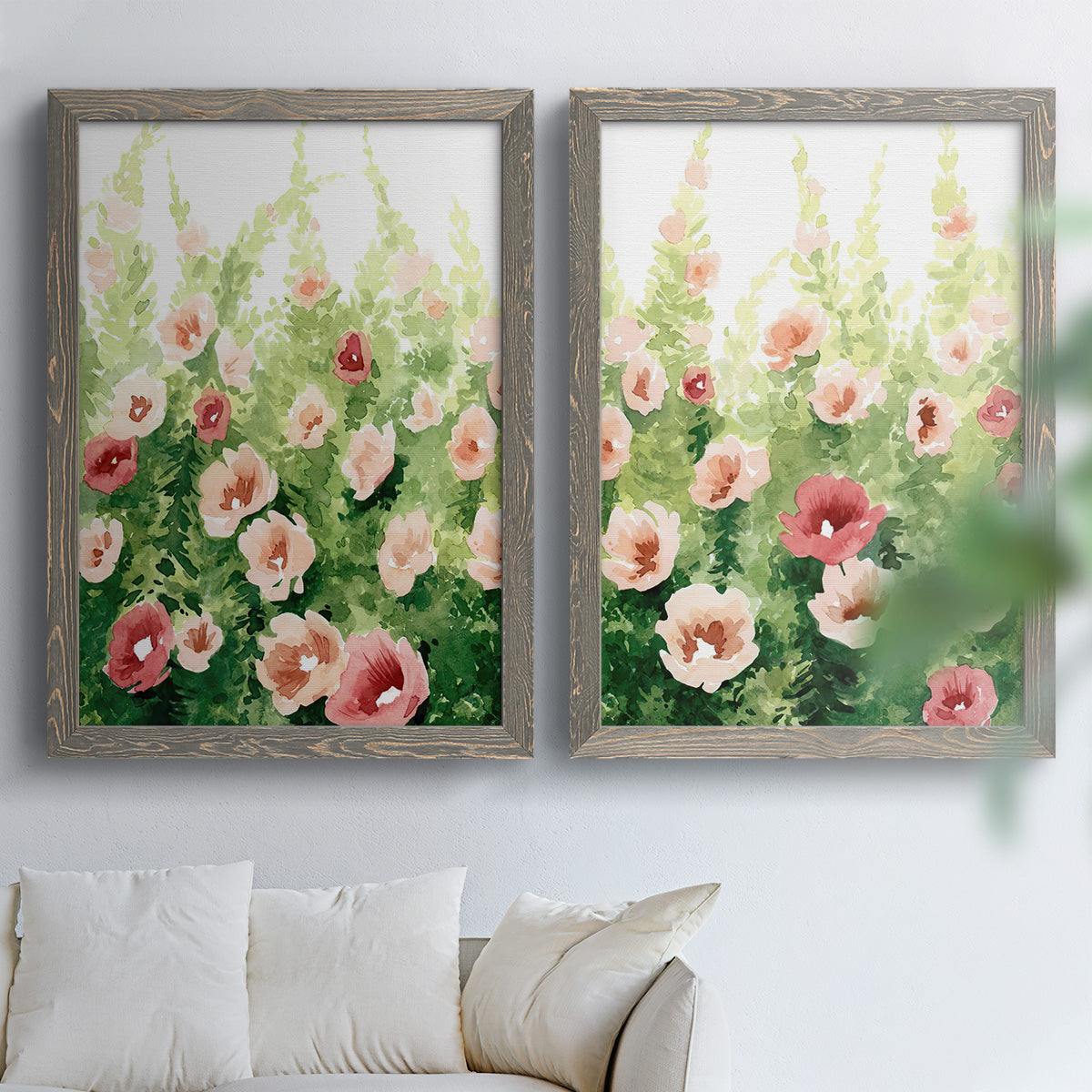 Set of two gray barnwood framed canvas prints depicting loose blossoms, green stems, and sunlit watercolor texture arranged across two complementary compositions above a sofa in a bright living space.